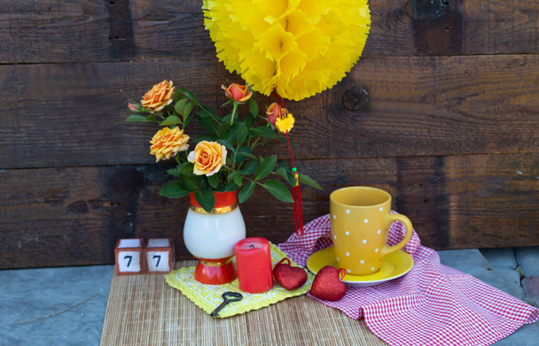 Una lanterna gialla cinese pende sul tavolo. Sul tavolo in un vaso ci sono rose, una tazza di tè, una candela e due cuori. Dietro ci sono due sette associati alla credenza di San Valentino cinese - Foto, immagini
