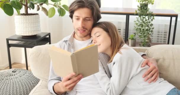 Man reading book to wife resting at home - Filmagem, Vídeo