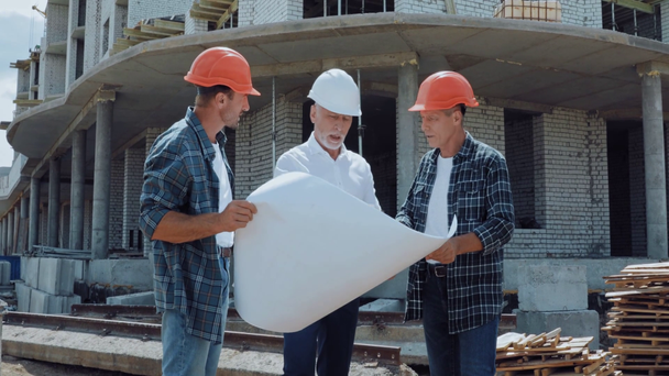 Engineer and builders discussing blueprint on construction site  - Metraje, vídeo