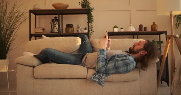 Sfrustrowany mężczyzna SMS-y na telefon komórkowy w domu - Materiał filmowy, wideo