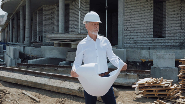 Красивый инженер в каскадной шляпе держит чертеж на строительной площадке - Кадры, видео