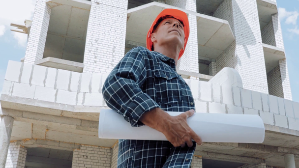 Builder with blueprint looking away on construction site - Séquence, vidéo