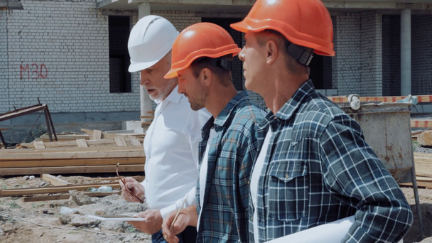 Engineer and builders with equipment talking while walking on construction site - Filmmaterial, Video