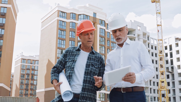 Engineer and builder with gadget and blueprint talking on construction site - Footage, Video