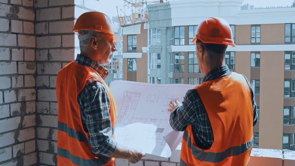 Constructores en chalecos de seguridad con plano hablando en el sitio de construcción - Imágenes, Vídeo