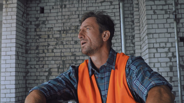 Vermoeide bouwer die een helm afdoet en glimlacht naar de camera op de bouwplaats - Video