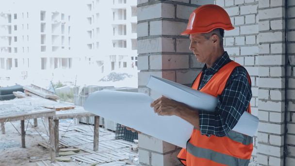 Комплексный строитель в шлеме смотрит на чертеж на строительной площадке - Кадры, видео