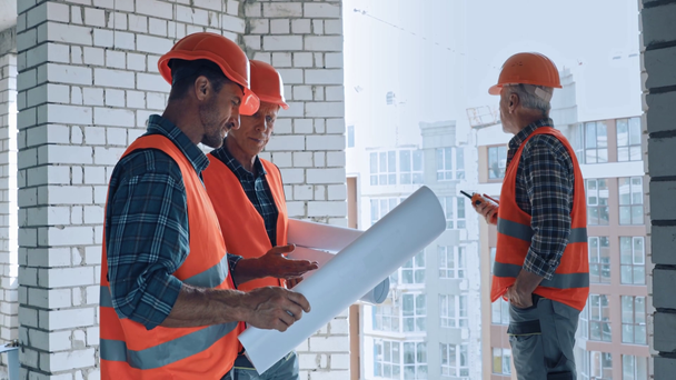 Constructeurs avec des plans et talkie walkie travaillant sur le chantier de construction - Séquence, vidéo