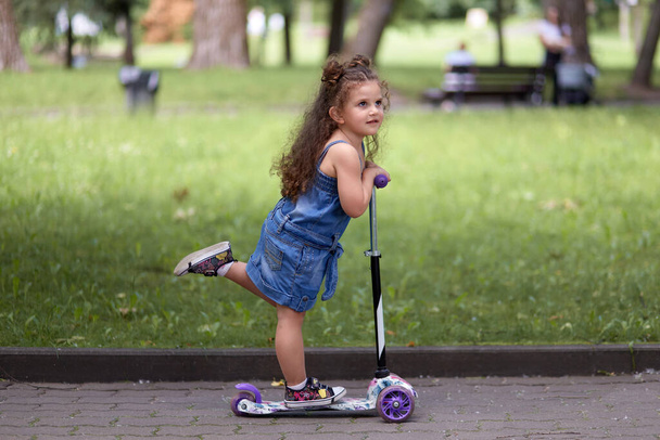 Happy beautiful cute little girl riding a scooter in the park. - Φωτογραφία, εικόνα