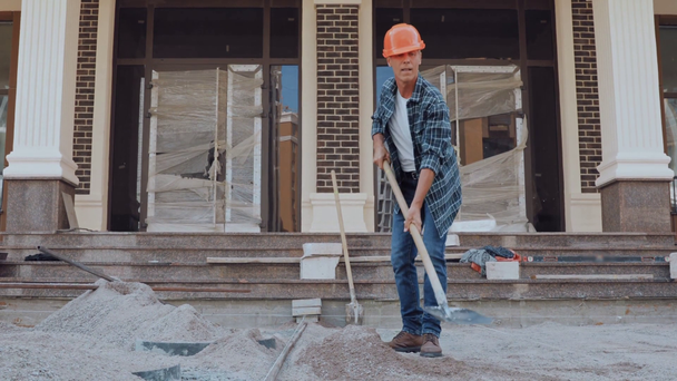 Constructor excavación de terreno con pala cerca de la construcción en el sitio de construcción - Metraje, vídeo