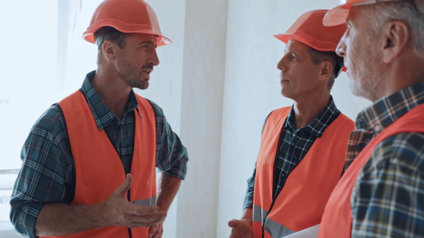 Bauarbeiter in Schutzhelmen und Westen sprechen auf Baustelle - Filmmaterial, Video