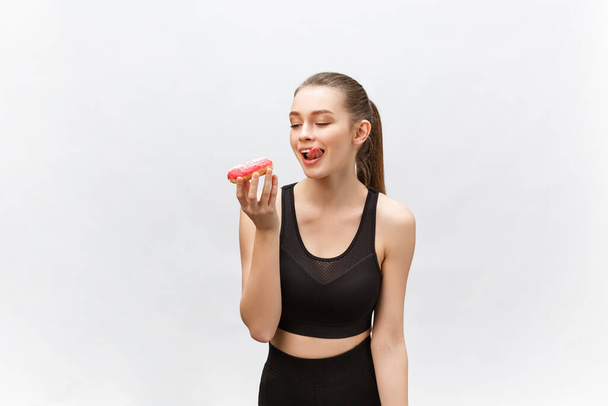 Beautiful Fitness model wearing a black fitness outfit holding a junk food donut. Isolated over grey background. - Φωτογραφία, εικόνα