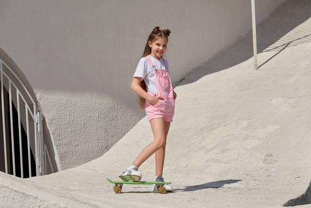 Beautiful slender girl with a skateboard on the background of a light building. - Fotó, kép