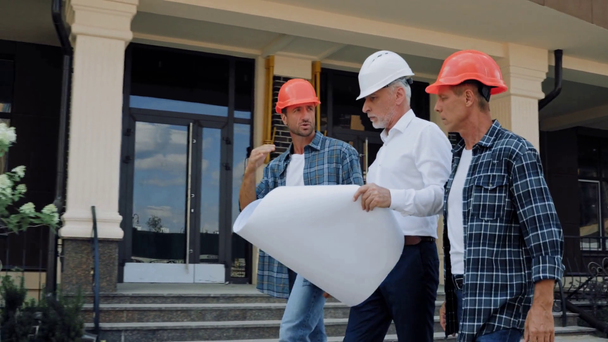 Ingeniero con proyecto y constructores caminando cerca de edificio en calle urbana
  - Metraje, vídeo