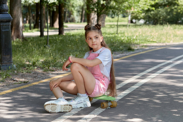 A cute beautiful girl is sitting on the track with a skateboard in her hands. - Φωτογραφία, εικόνα