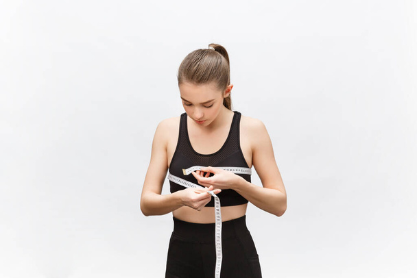 Jeune femme avec un excès de poids en haut sportif regardant tristement sur le résultat de mesurer la taille sur fond blanc - Photo, image