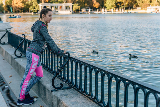 Chica rubia en ropa de fitness hace un descanso junto al lago con patos un día de otoño
 - Foto, imagen