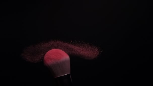 Szczotka do makijażu rozprzestrzeniania różowy rumieniec proszek na czarnym tle. zwolniony ruch  - Materiał filmowy, wideo
