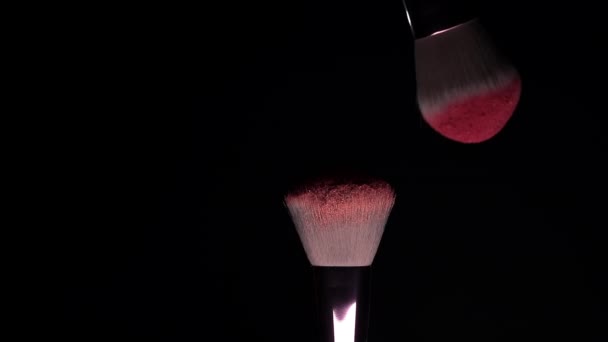 暗い背景にピンクの粉を持つ2つのメイクブラシ - 映像、動画