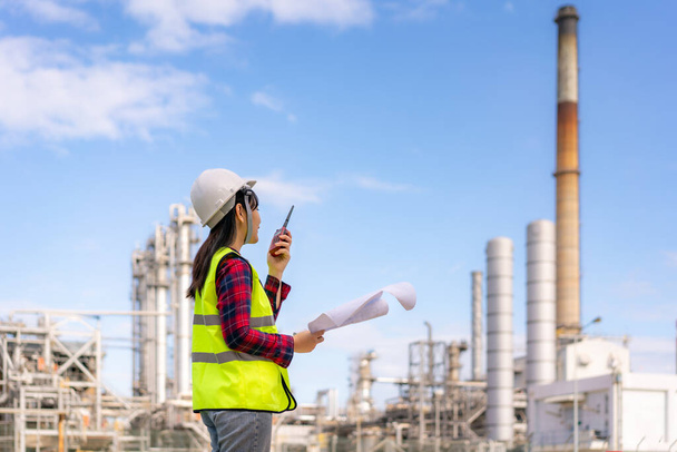 Asian woman technician Industrial engineer using walkie-talkie and holding bluprint working in oil refinery for building site survey in civil engineering project. - Foto, imagen