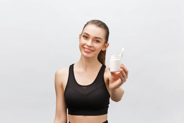 Smiling blonde sport woman holding bottle of medicine on white background - Photo, image