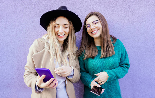 Portrait de deux jeunes amis utilisant leur téléphone portable en violet - Photo, image