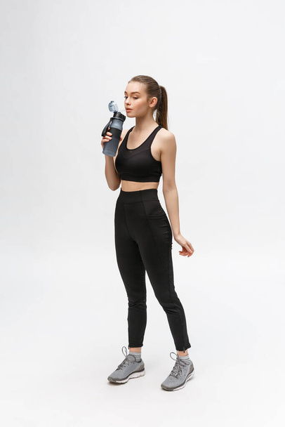Side view full length portrait of a young healthy sports woman holding a water bottle isolated on a white background - Photo, Image