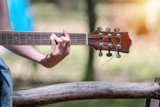 Hands of young woman holding acoustic guitar on nature background. Guitarist young girl playing guitar while sitting on the camp with copy space.  - Photo, Image