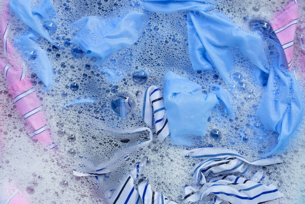 Vista superior de roupas coloridas mergulhar em dissolução de água detergente em pó. Conceito de roupa
 - Foto, Imagem