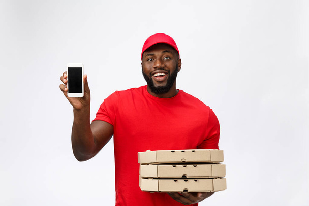 Delivery Concept: Knappe Afrikaanse pizzabezorger in gesprek met mobiel met schokkende gezichtsuitdrukking. Geïsoleerd over grijze achtergrond. - Foto, afbeelding