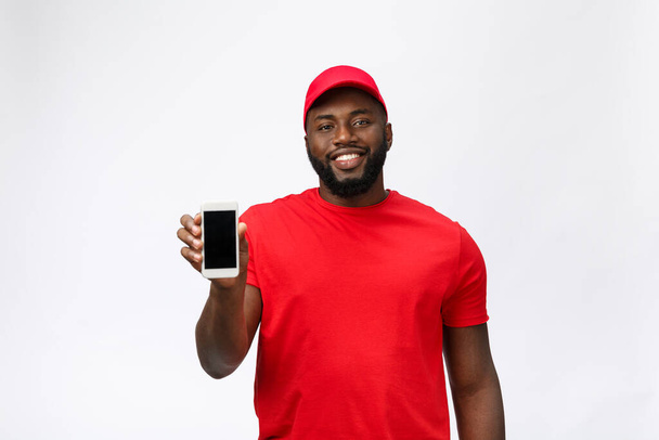 Delivery Concept - Portret van Handsome Afro-Amerikaanse bezorger of koerier toont mobiele telefoon op u om de bestelling te controleren. Geïsoleerd op Grey Studio Achtergrond. Kopieer ruimte. - Foto, afbeelding
