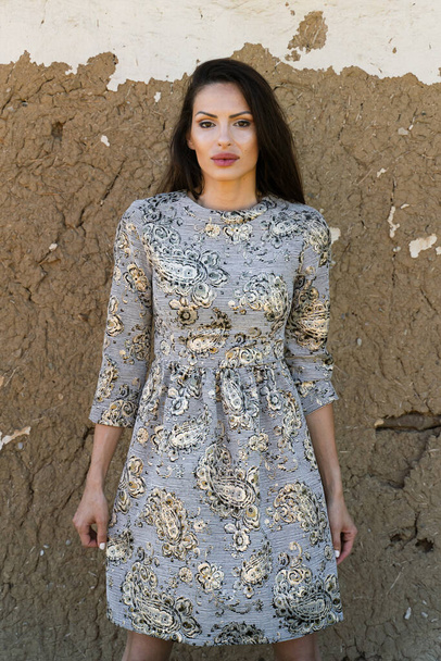 Front view portrait of caucasian woman wearing dress standing in front of the wall of traditional house made of dirt and clay looking to the camera - identity solitude loneliness concept - Foto, Imagen