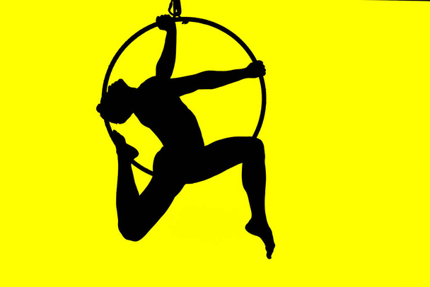 silhouette of man in tall acrobatic hoop with elegant pose and yellow illuminated background - Photo, Image