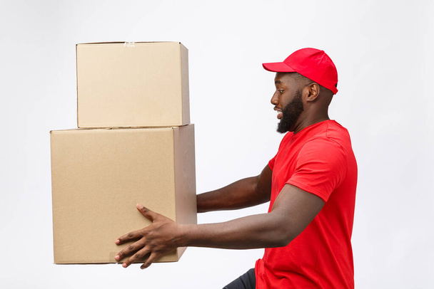 Retrato da entrega homem americano africano em camisa vermelha. ele levantando caixas de peso pesado contra ter um isolado no fundo branco
. - Foto, Imagem