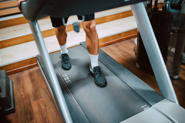 Крупним планом ноги молодого м'язово-кавказького спортсмена, який тренується і біжить на біговій доріжці в тренажерному залі. Захист від COVID 19 коронавірусу
 - Фото, зображення