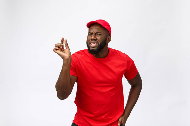 Delivery Concept - Portrait of Serious African American delivery man bemutató buta agresszív kifejezés és boldogtalan. Elszigetelve a szürke stúdió hátterében. Fénymásolási tér. - Fotó, kép