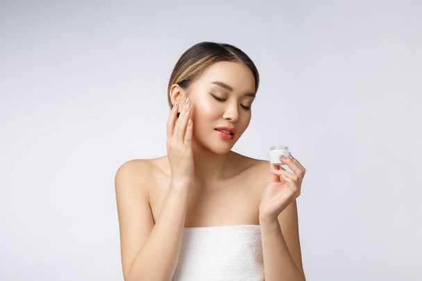 Asiatin trägt kosmetische Creme auf die Haut auf isoliertem weißem Hintergrund auf - Foto, Bild