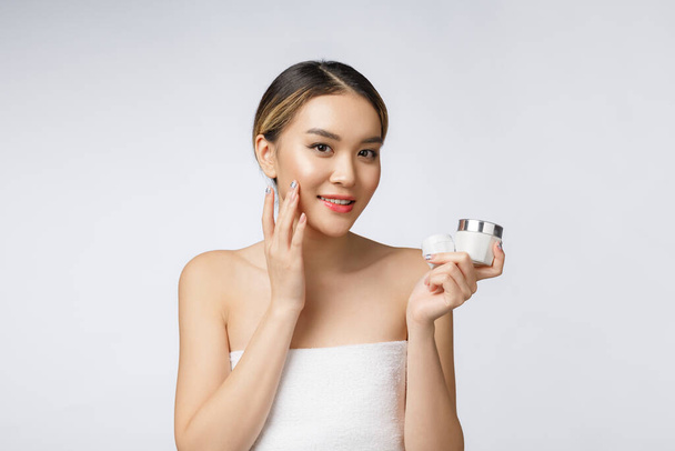 Femme asiatique appliquant la crème cosmétique sur la peau sur fond blanc isolé - Photo, image