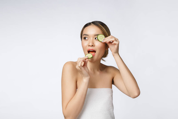 Beyaz arka planda izole edilmiş ellerinde salatalık dilimi tutan ve yiyen genç Asyalı kadın. - Fotoğraf, Görsel