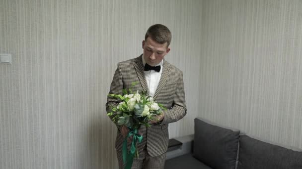 Groom with wedding bouquet in his hands at home. White shirt, jacket - Filmati, video