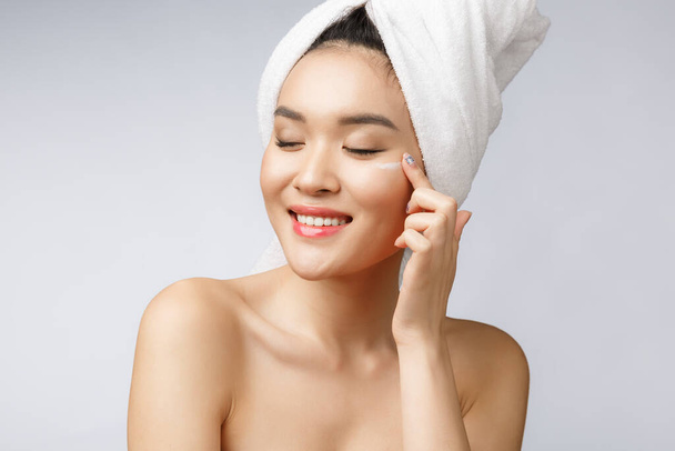 zdrowie i uroda - Atrakcyjna Azjatka nakładająca krem na skórę, odizolowana na biało. - Zdjęcie, obraz