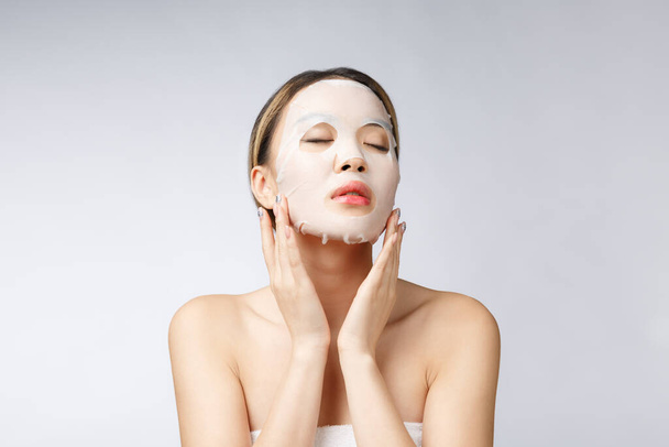 Belle femme asiatique appliquant masque feuille de papier sur son visage fond blanc - Photo, image