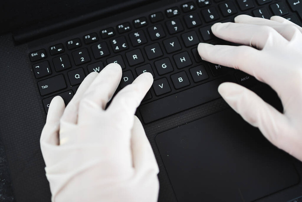 the new normal after thecovid-19 virus pandemic outbreak, hands typing on shared computer keyboard at work wearing disposable gloves to avoid contact with potentially infected surfaces - 写真・画像