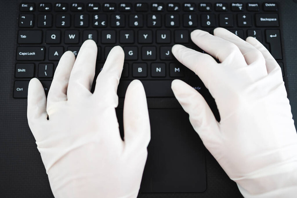 the new normal after thecovid-19 virus pandemic outbreak, hands typing on shared computer keyboard at work wearing disposable gloves to avoid contact with potentially infected surfaces - Photo, image