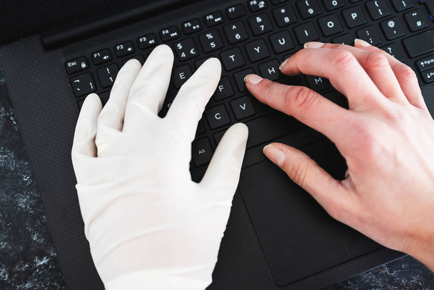 staying safe after the covid-19 virus pandemic outbreak, hand typing on shared computer keyboard at work wearing disposable glove to avoid contact with potentially infected surfaces and other hand without glove - Фото, зображення