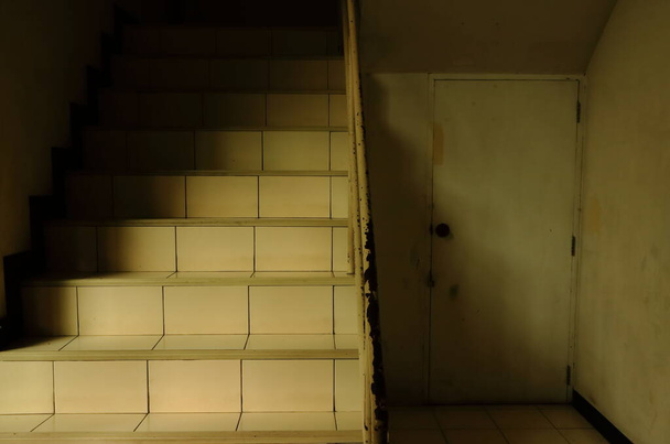Silent stairs with sunlight and shadow next to closed storeroom under staircase, low angle view   - Photo, Image