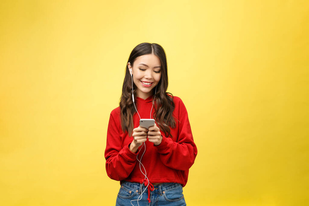 Portrait of a happy woman listening music in earphones and dancing isolated on a yellow background - Photo, Image