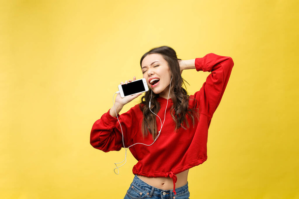 Portrait of a happy woman listening music in earphones and dancing isolated on a yellow background - Foto, afbeelding