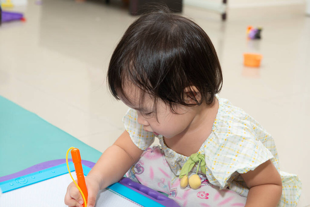 niña jugando con el tablero de dibujo magnético en el suelo
 - Foto, Imagen