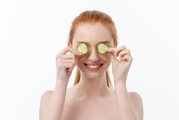 Close up beauty portrait of a smiling beautiful half naked woman holding cucumber slices at her face isolated over white background - 写真・画像